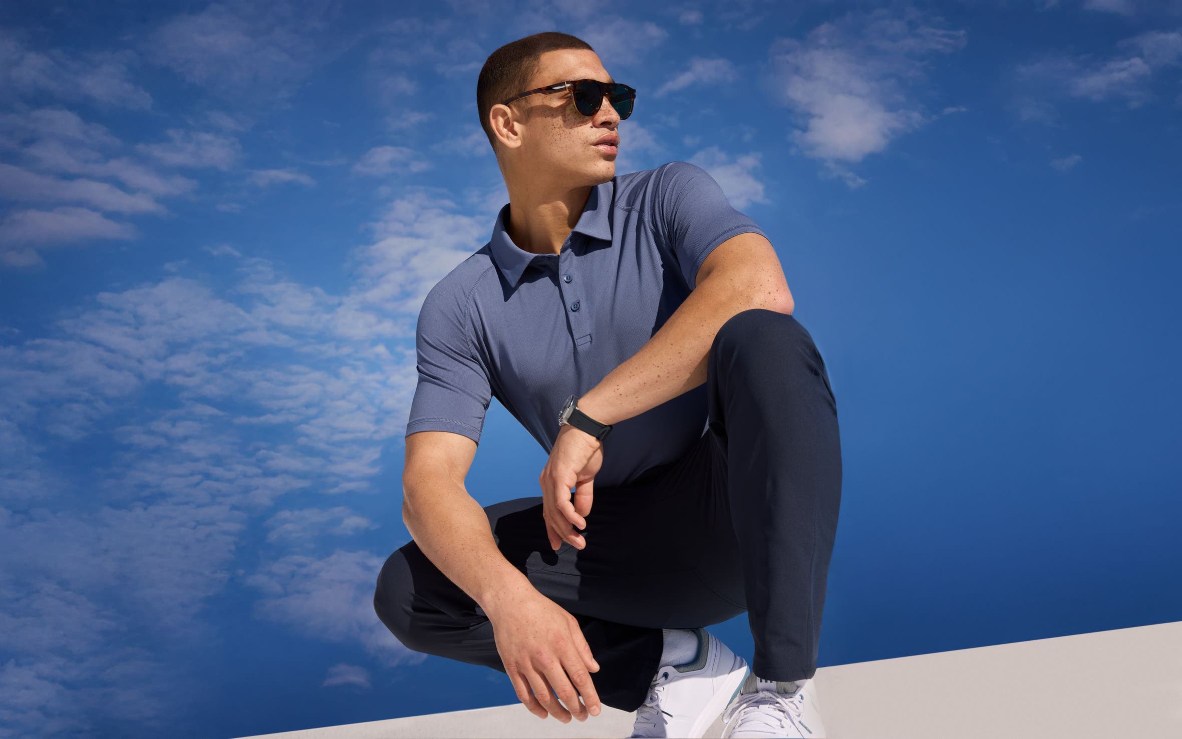 A man wearing a blue-grey polo shirt and navy pants.