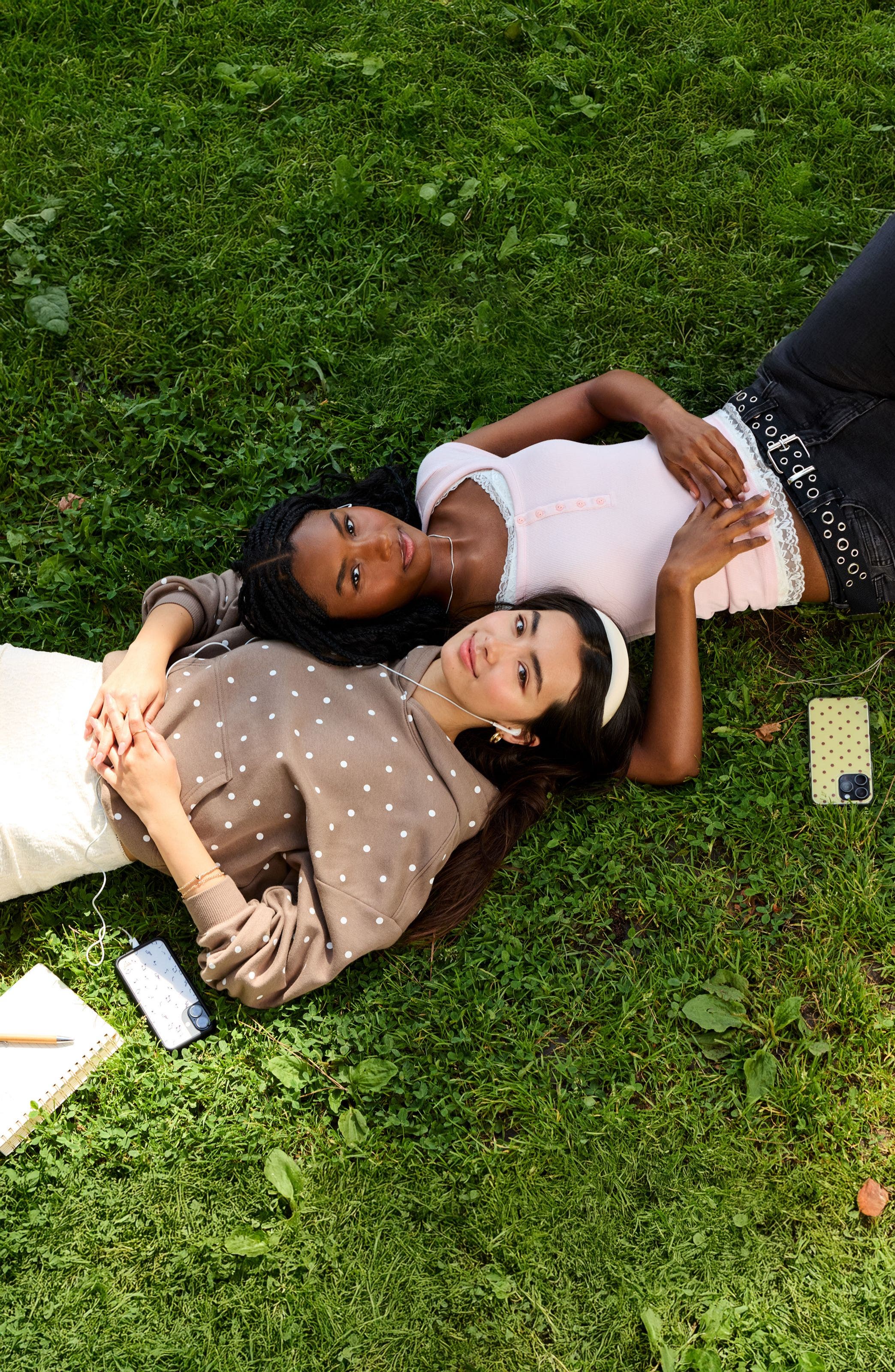 Two girls laying in the grass wearing back to campus style clothing.
