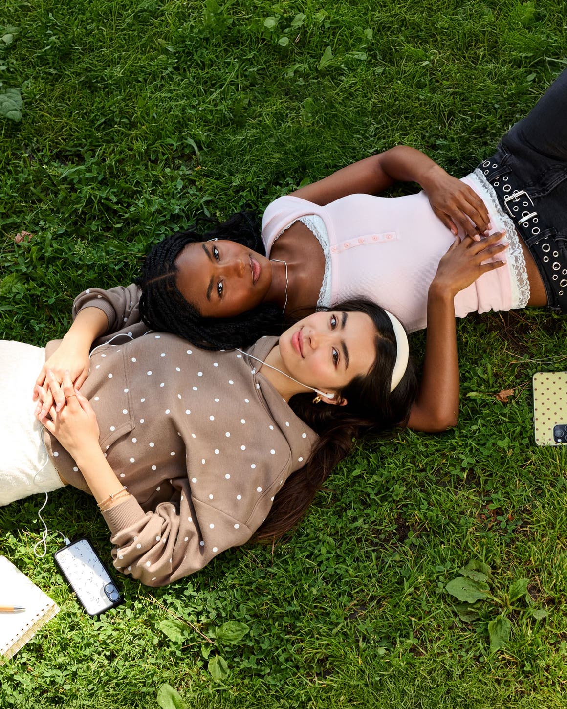 Two girls laying in the grass wearing back to campus style clothing.