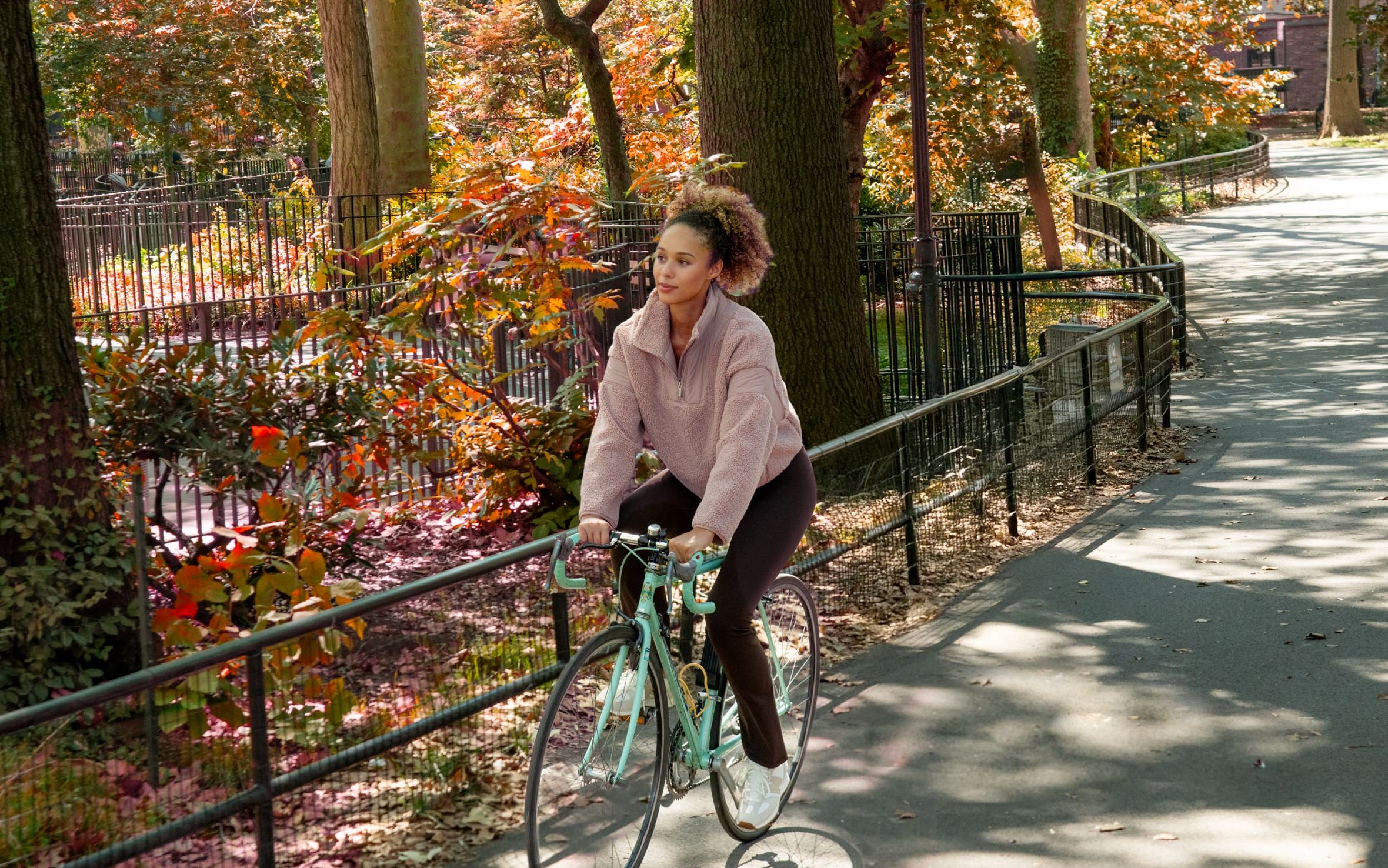 A woman riding a bike wearing a faux shearling pullover, leggings and sneakers.