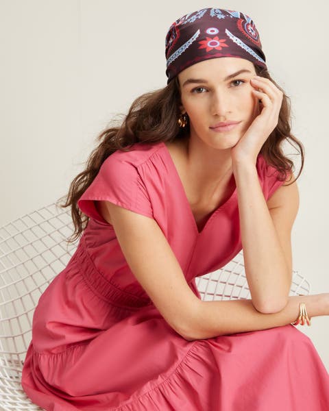 A woman wearing a pink tiered dress and patterned headscarf.