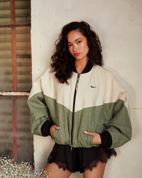 Woman wearing a cream and green colorblock Nike jacket and black lace skirt.