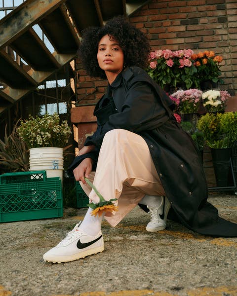 Woman wearing white Nike sneakers with cream pants and a black oversized coat.