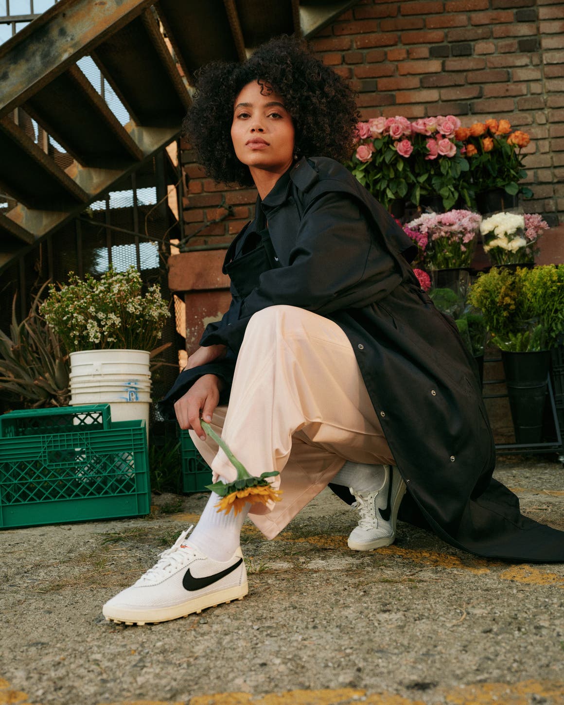 Woman wearing white Nike sneakers with cream pants and a black oversized coat.