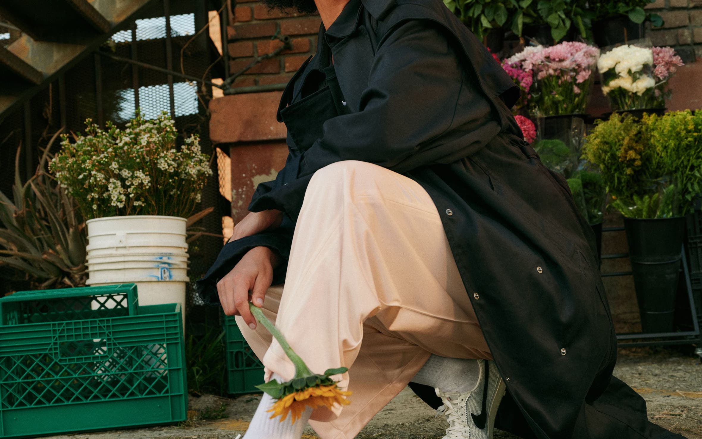 Woman wearing white Nike sneakers with cream pants and a black oversized coat.