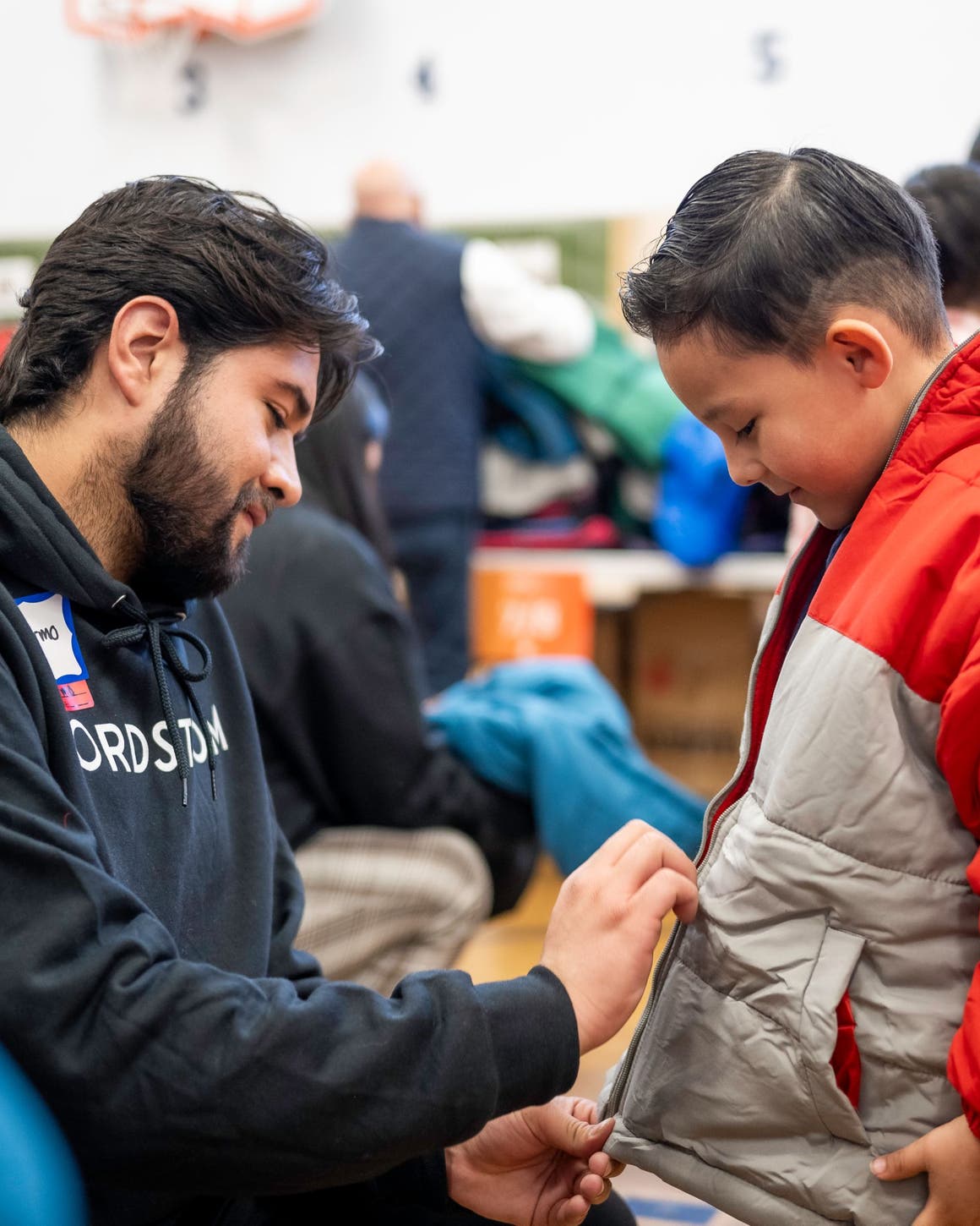 A Nordstrom employee helping a boy zip up his new coat.