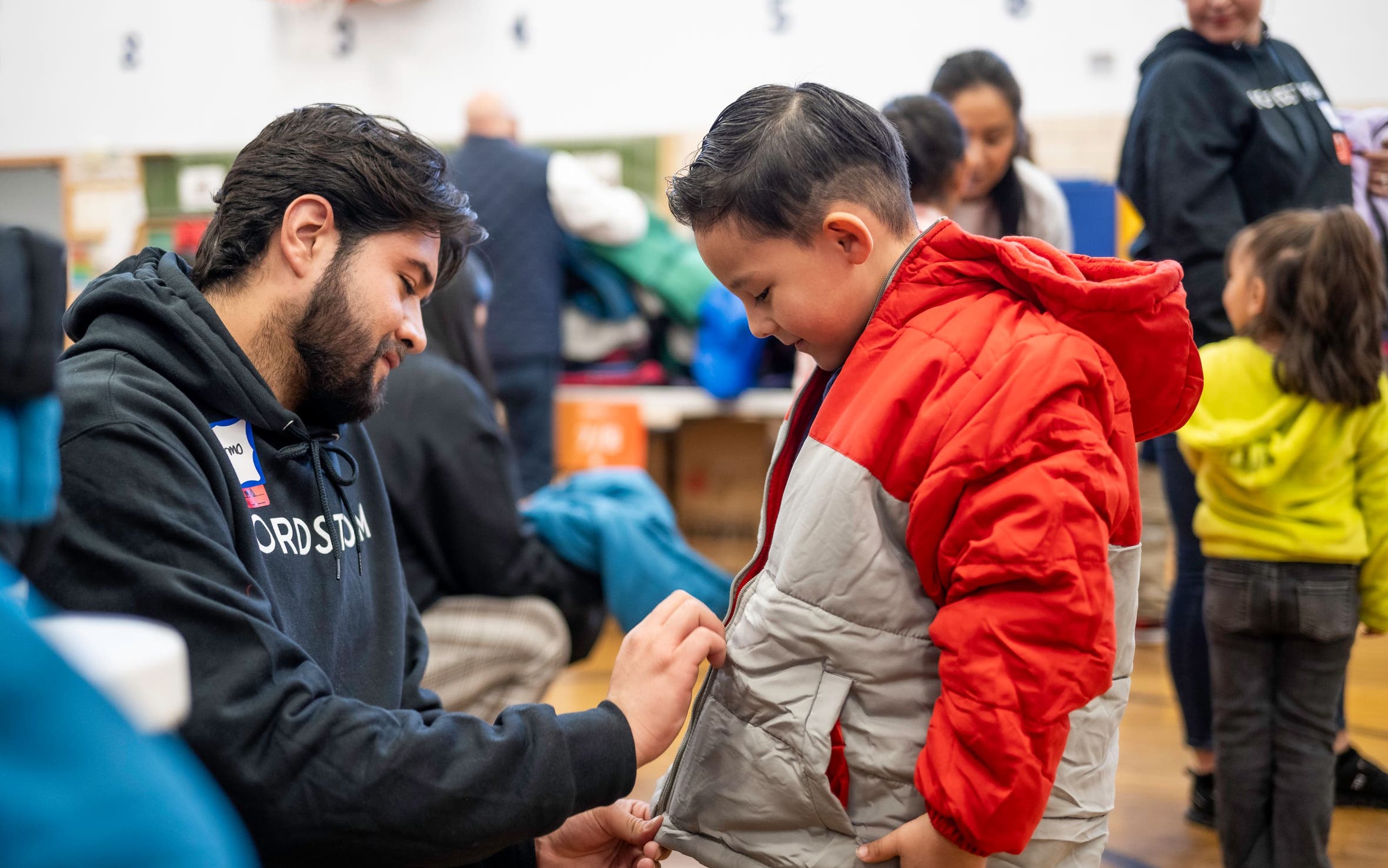 A Nordstrom employee helping a boy zip up his new coat.