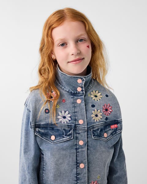 A girl wearing a denim jacket with floral embroidery.