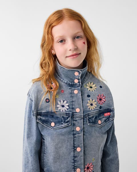 A girl wearing a denim jacket with floral embroidery.