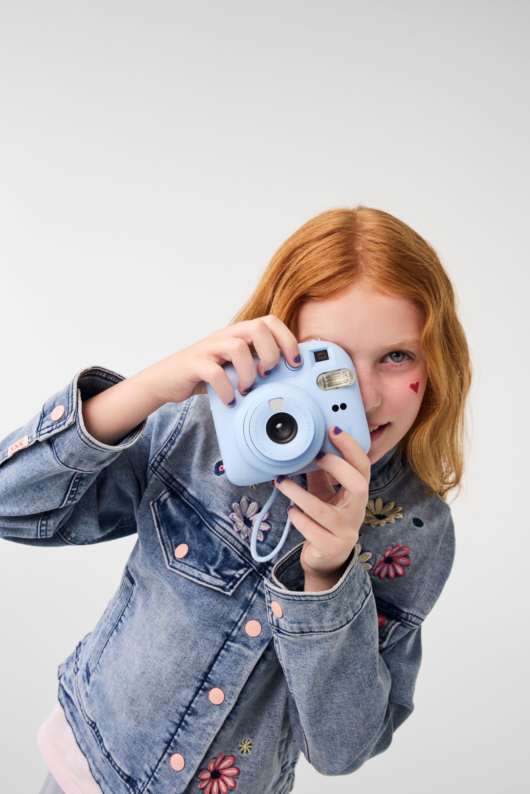 A girl wearing a denim jacket poses with a camera.