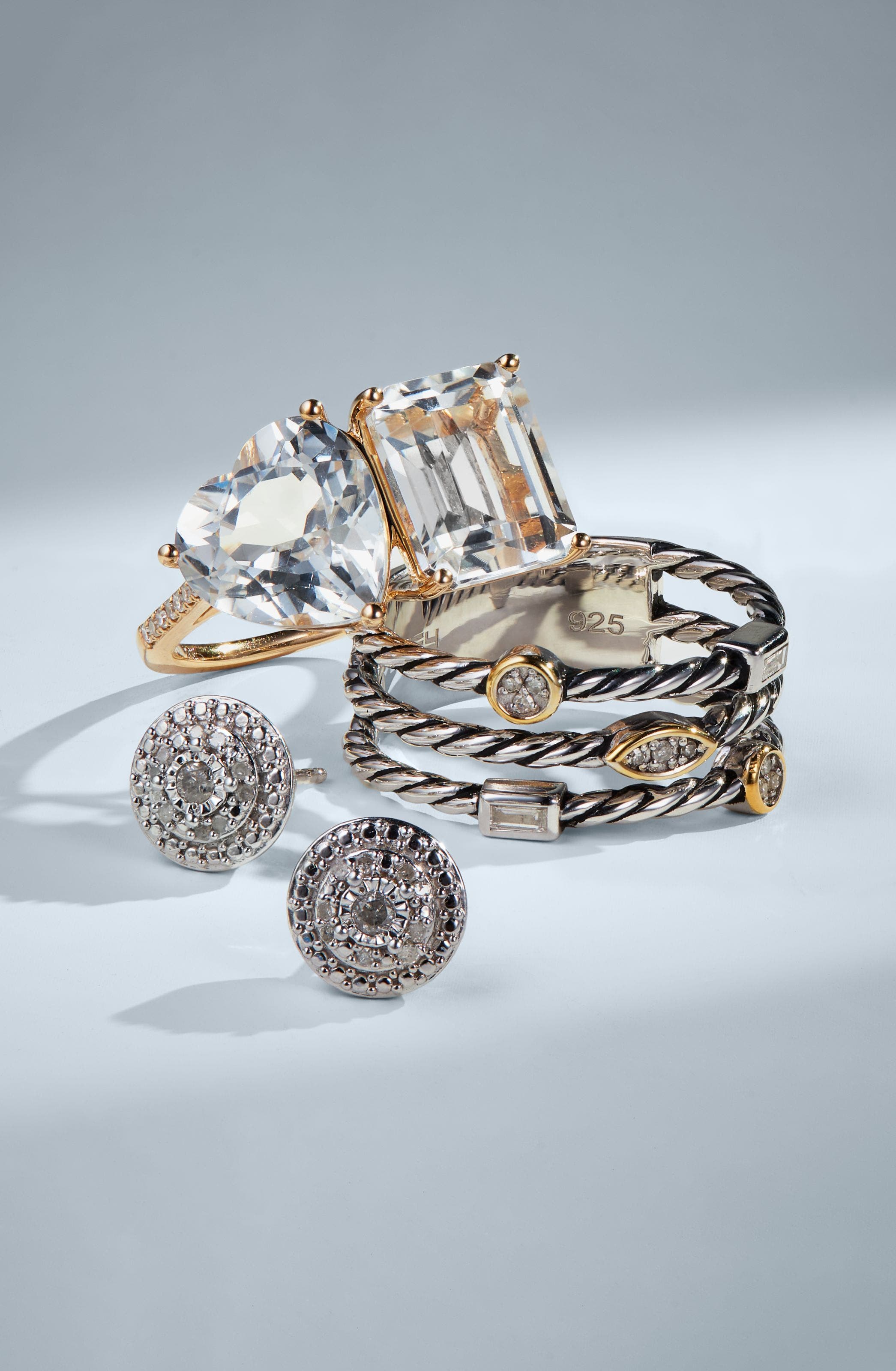 Fine jewelry flat lay featuring crystal statement rings, silver cable stacking rings, and diamond pave stud earrings.