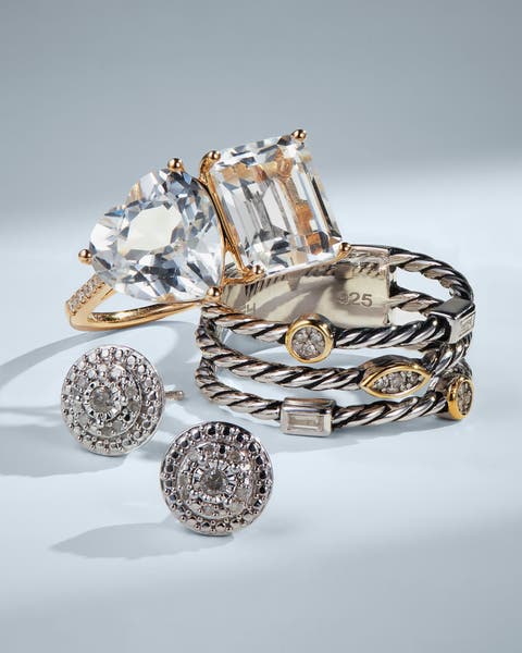 Fine jewelry flat lay featuring crystal statement rings, silver cable stacking rings, and diamond pave stud earrings.