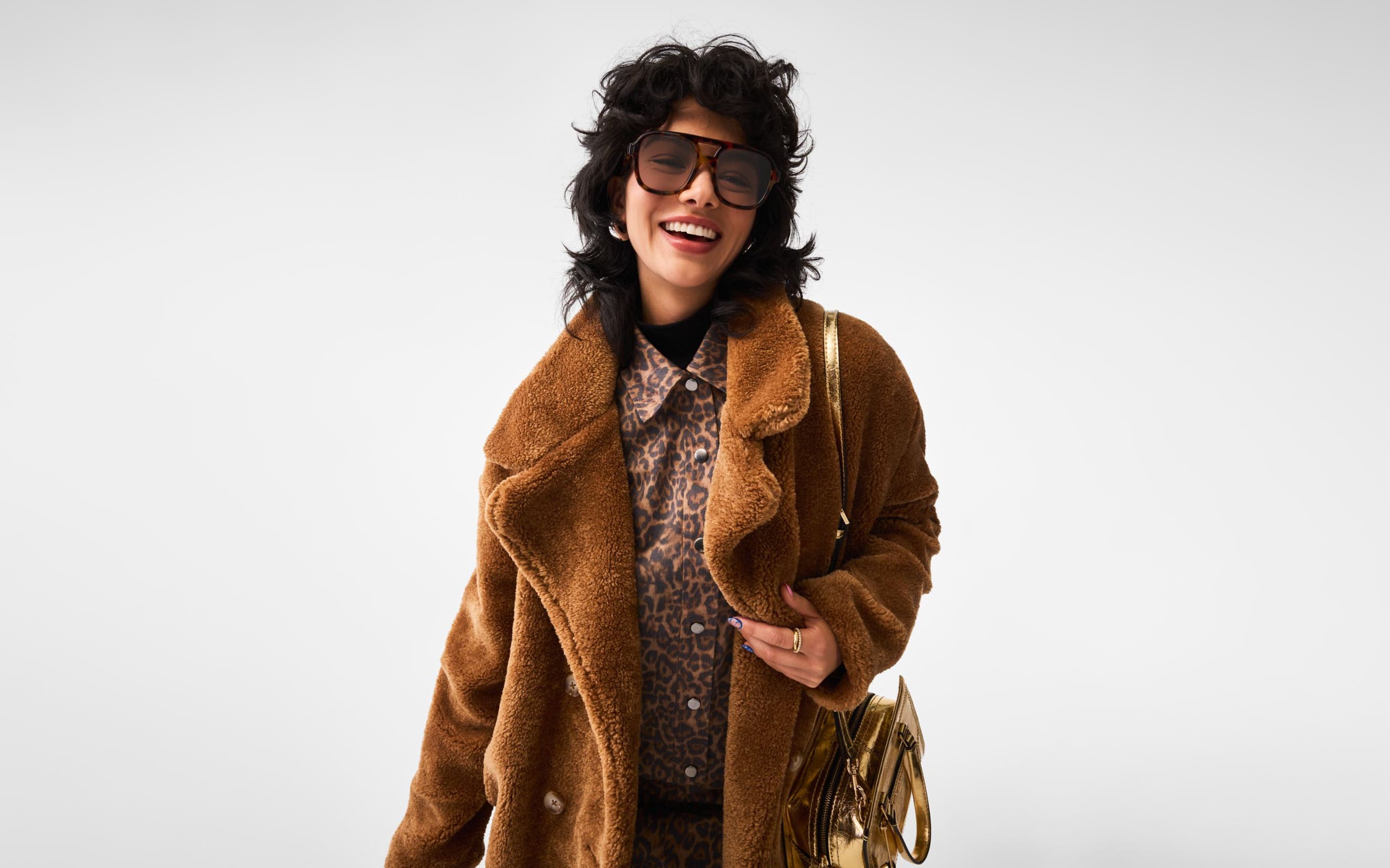 A woman carrying a gold handbag and wearing sunglasses, an animal-print shirt and a faux-fur coat. 