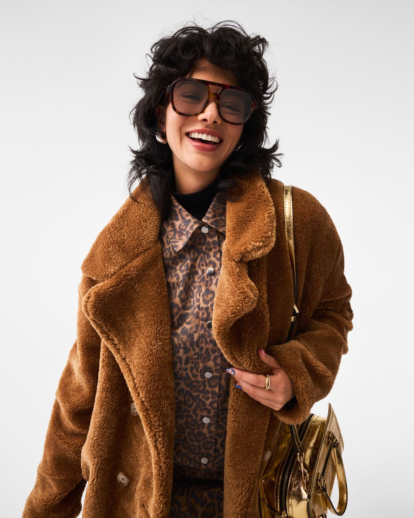 A woman carrying a gold handbag and wearing sunglasses, an animal-print shirt and a faux-fur coat.