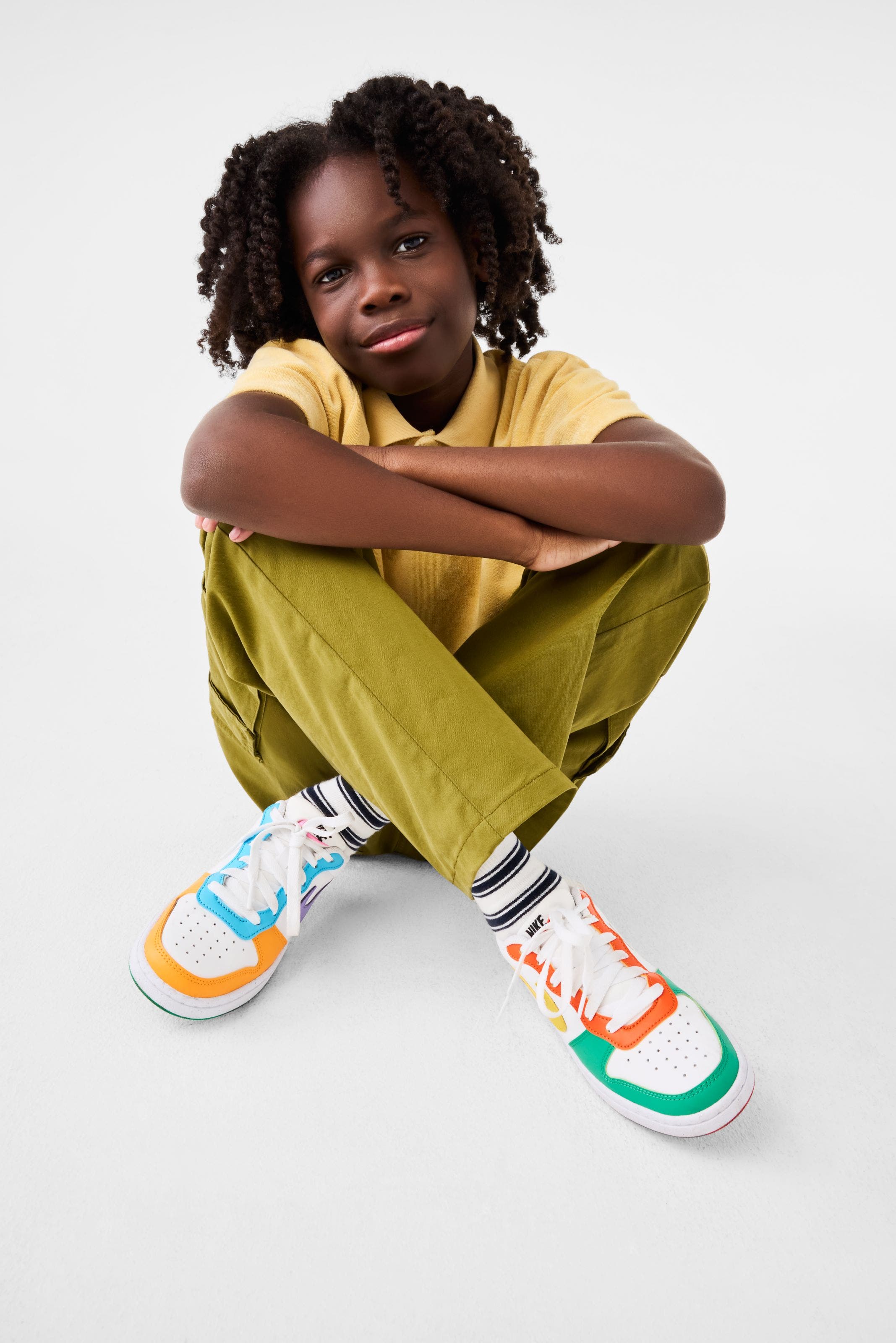 A child wearing a yellow polo, green pants and colorful sneakers.