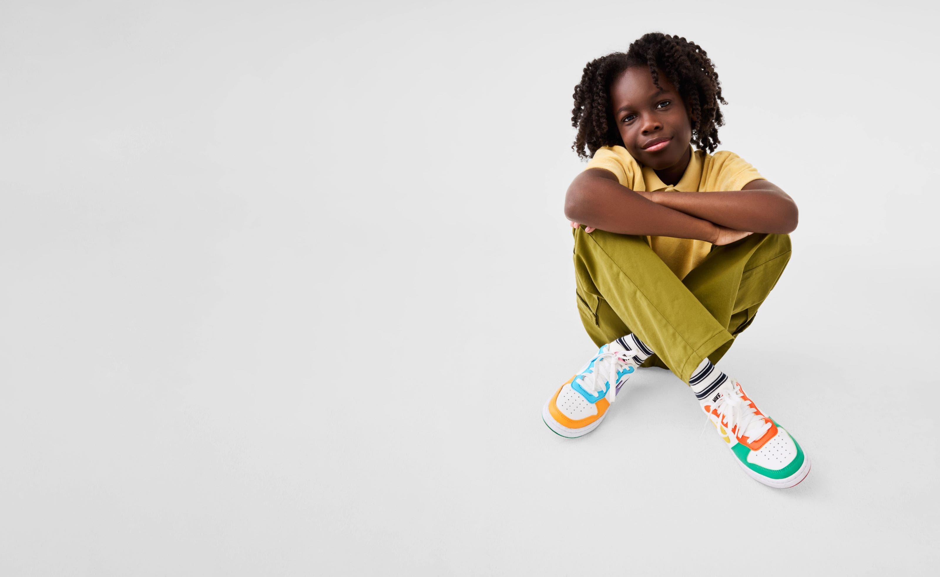A child wearing a yellow polo, green pants and colorful sneakers.