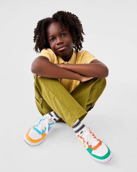A boy wearing a yellow polo, green pants and colorful sneakers.