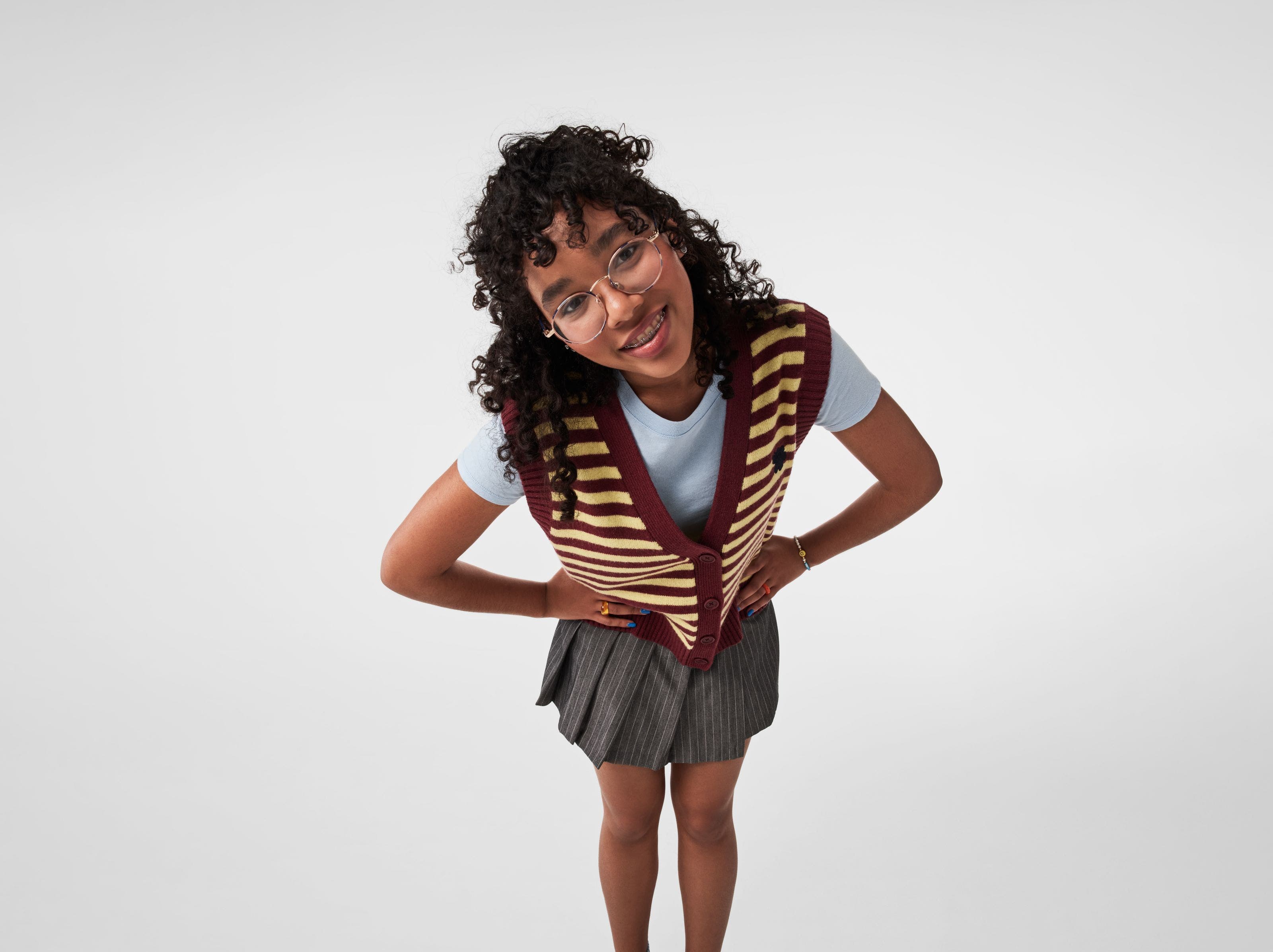 A girl wearing a striped vest with a T-shirt and a pleated skirt.