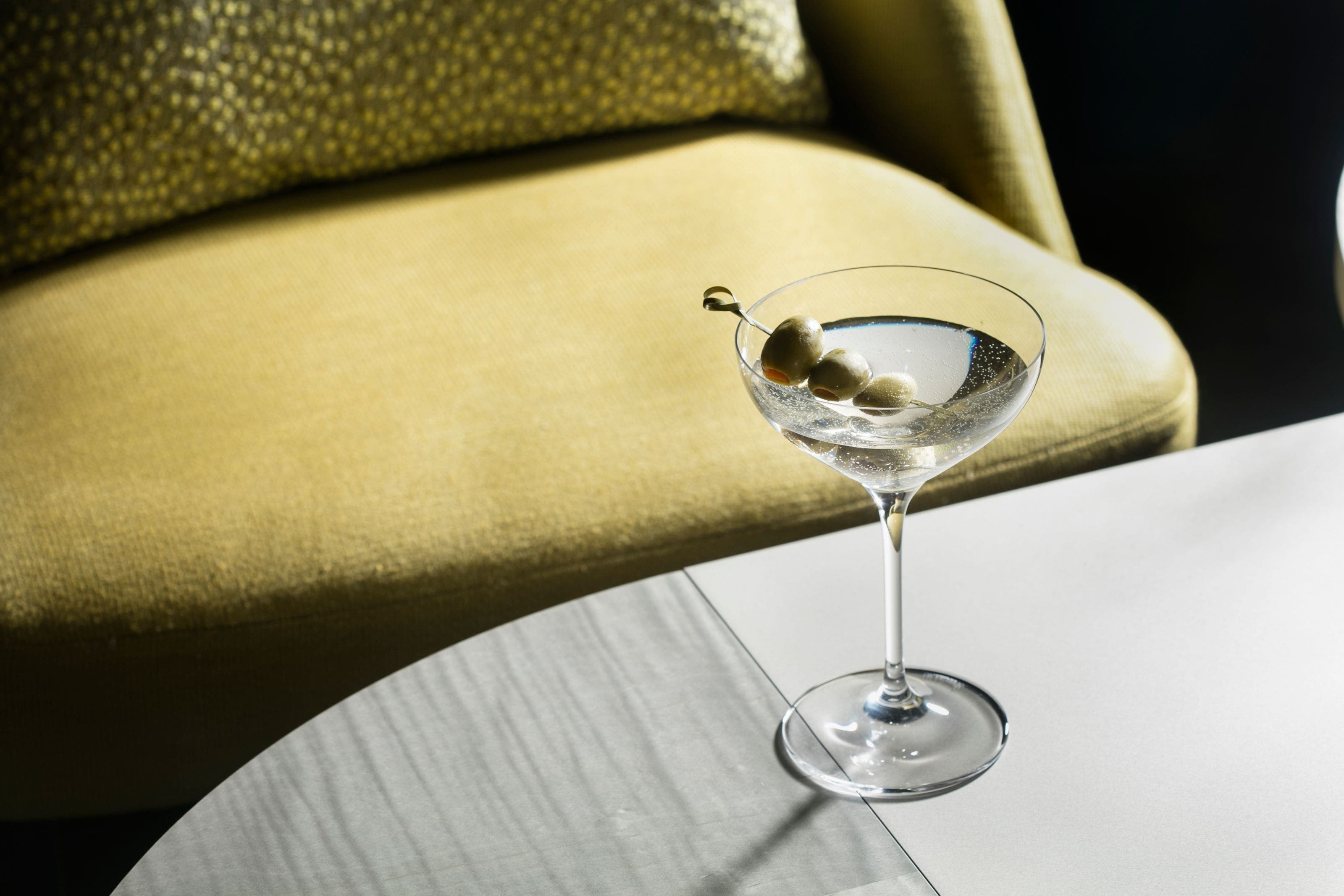 A martini with three olives on a bar. 