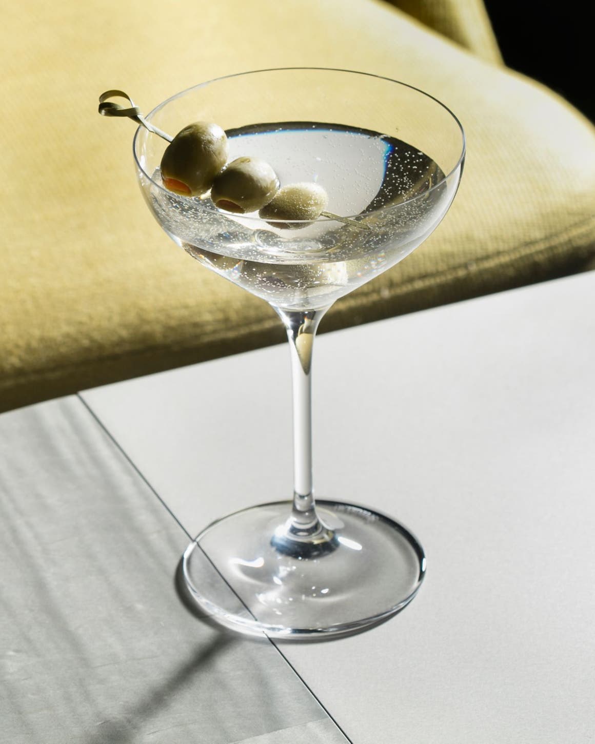 A martini with three olives on a bar.