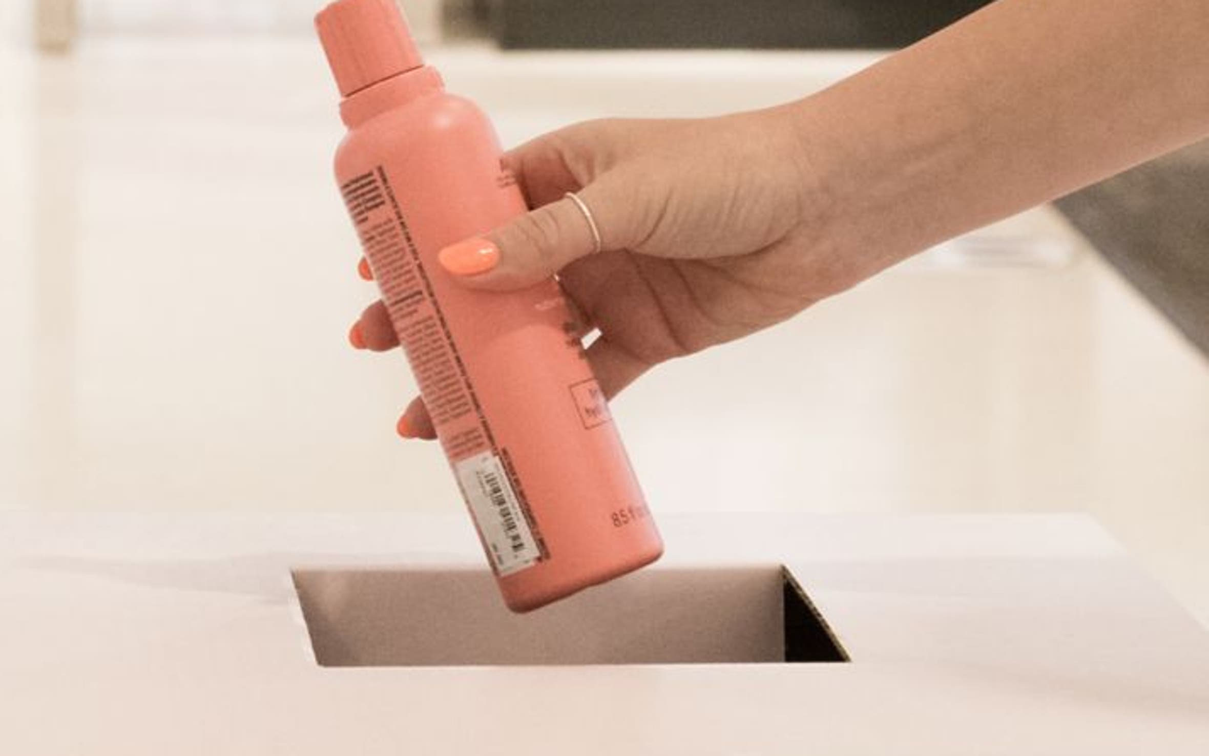 An empty shampoo bottle being placed in a BeautyCycle bin.
