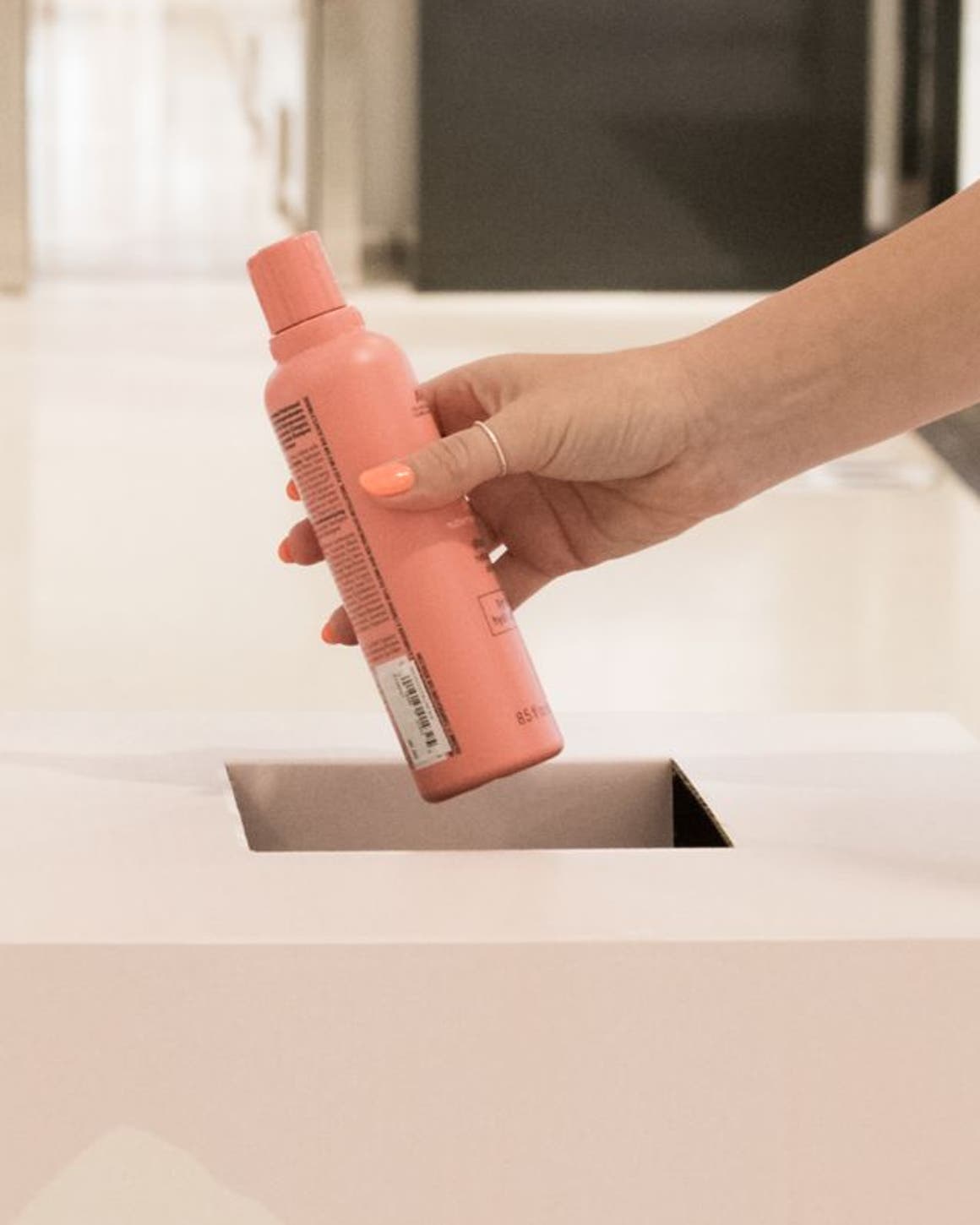 An empty shampoo bottle being placed in a BeautyCycle bin.