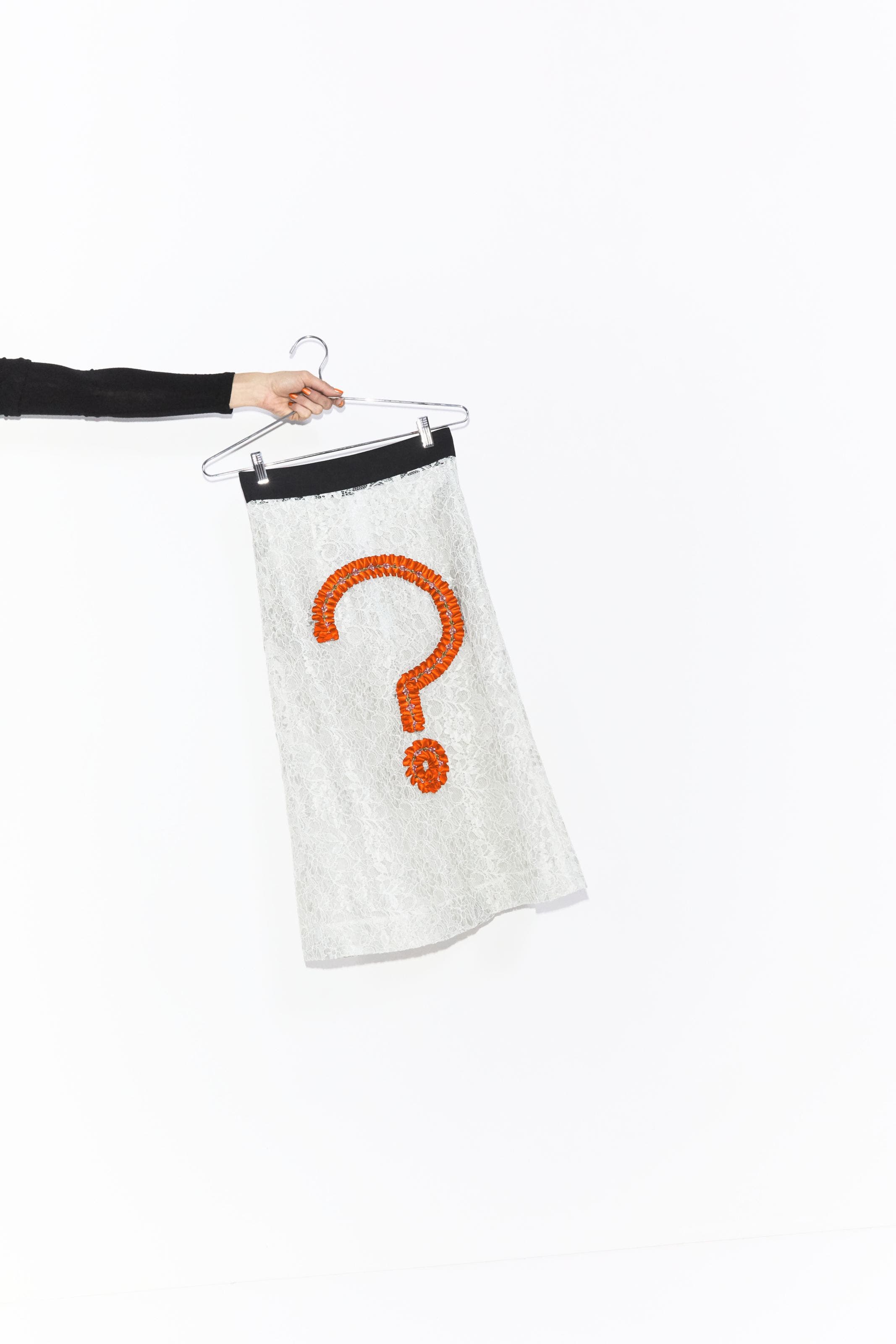 A person holding a skirt embellished with a question mark on a hanger. 