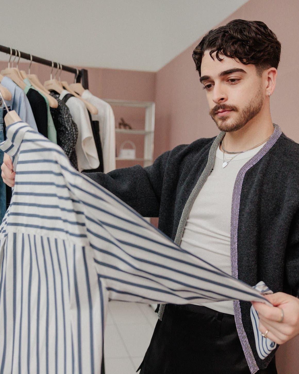 A man examining a striped shirt in front of a rack of clothing.