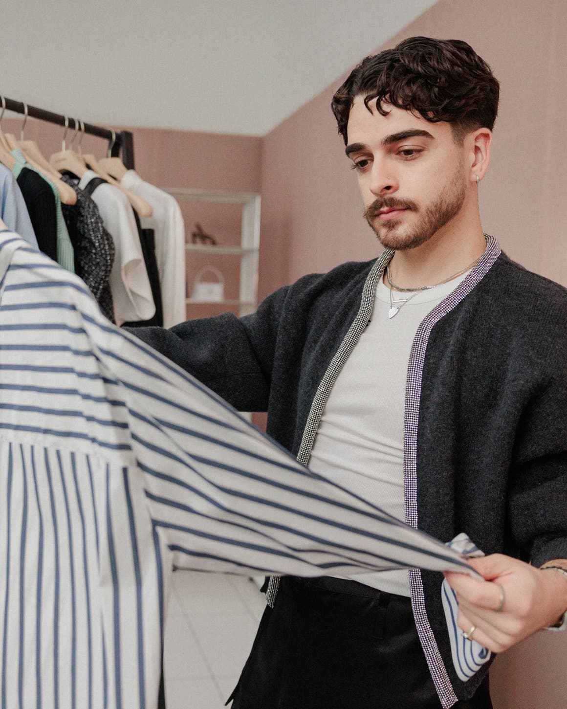 A man examining a striped shirt in front of a rack of clothing.