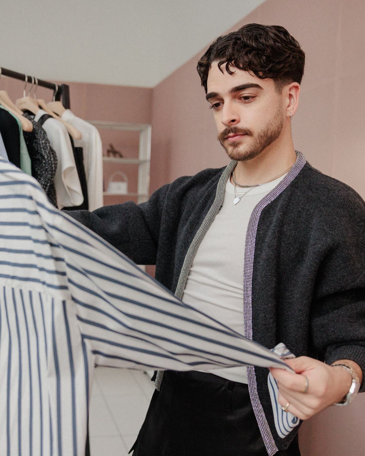 A man examining a striped shirt in front of a rack of clothing.