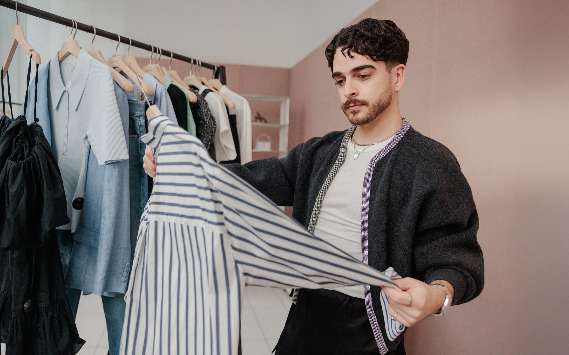 A man examining a striped shirt in front of a rack of clothing.