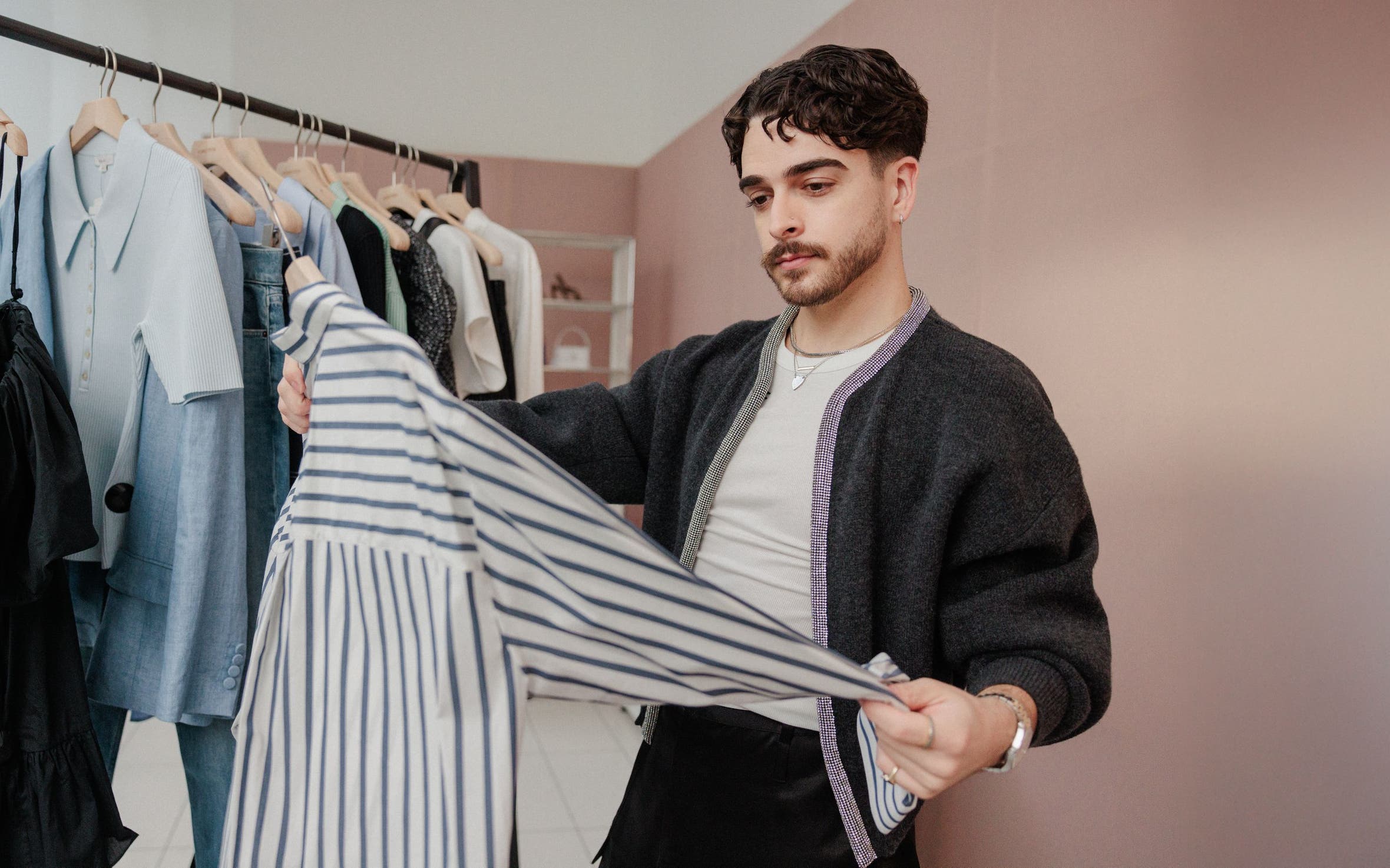 A man examining a striped shirt in front of a rack of clothing.