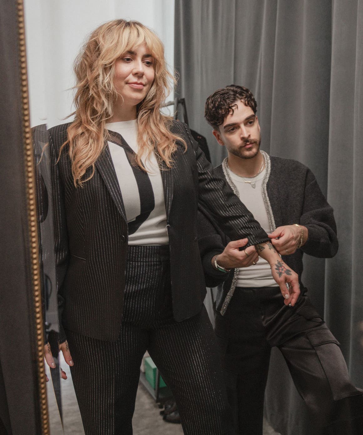 A stylist helping a woman adjust the sleeve length of her jacket.