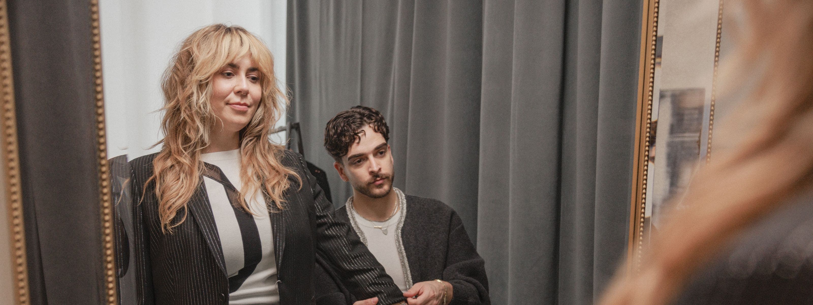 A stylist helping a woman adjust the sleeve length of her jacket.