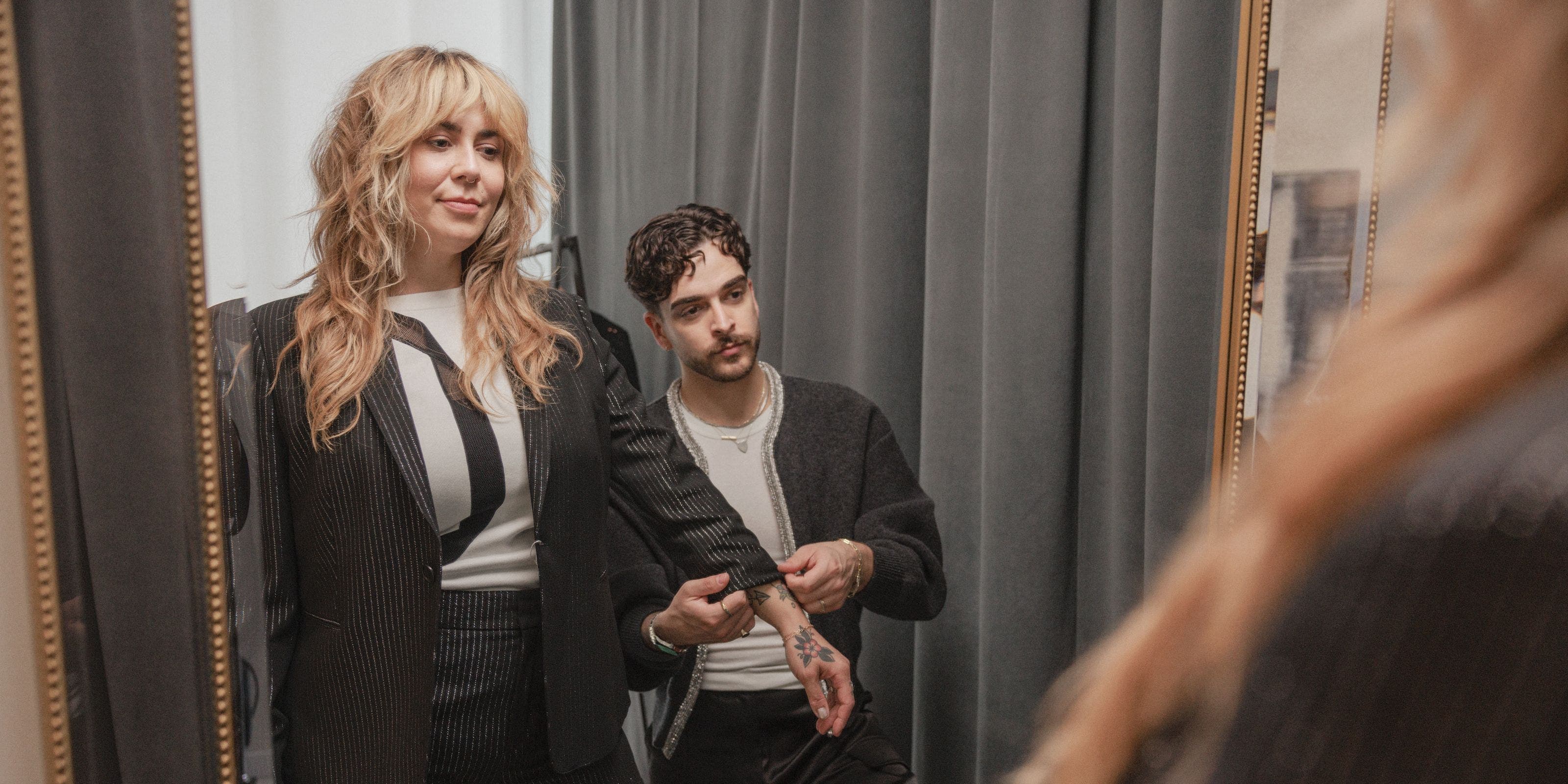 A stylist adjusting a woman's sleeve.