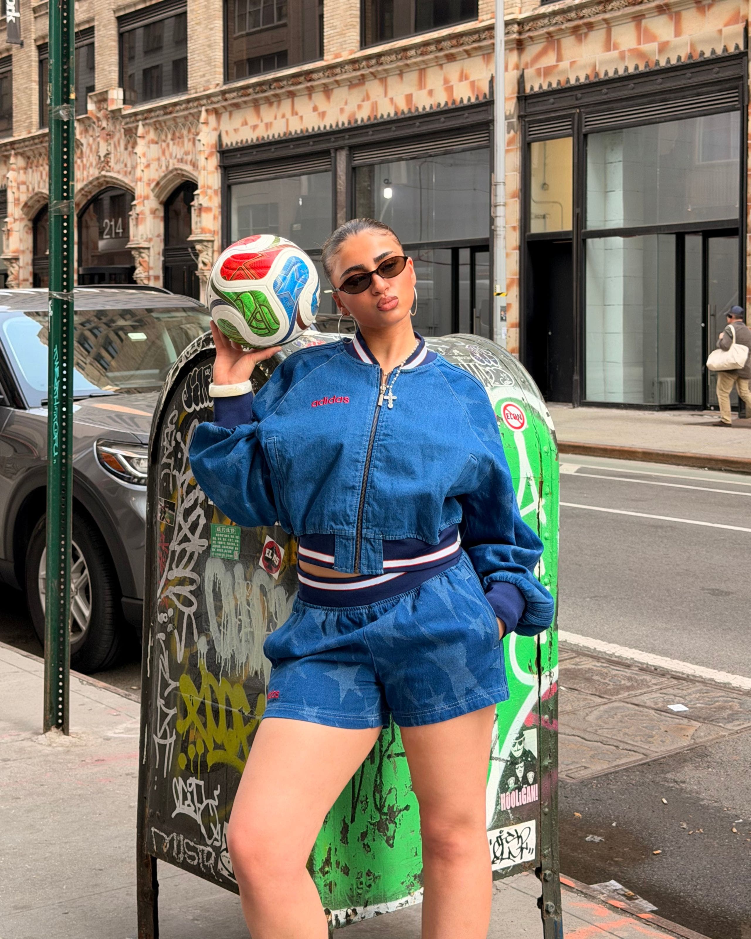 Woman wearing a blue varsity jacket and blue shorts, holding a soccer ball.
