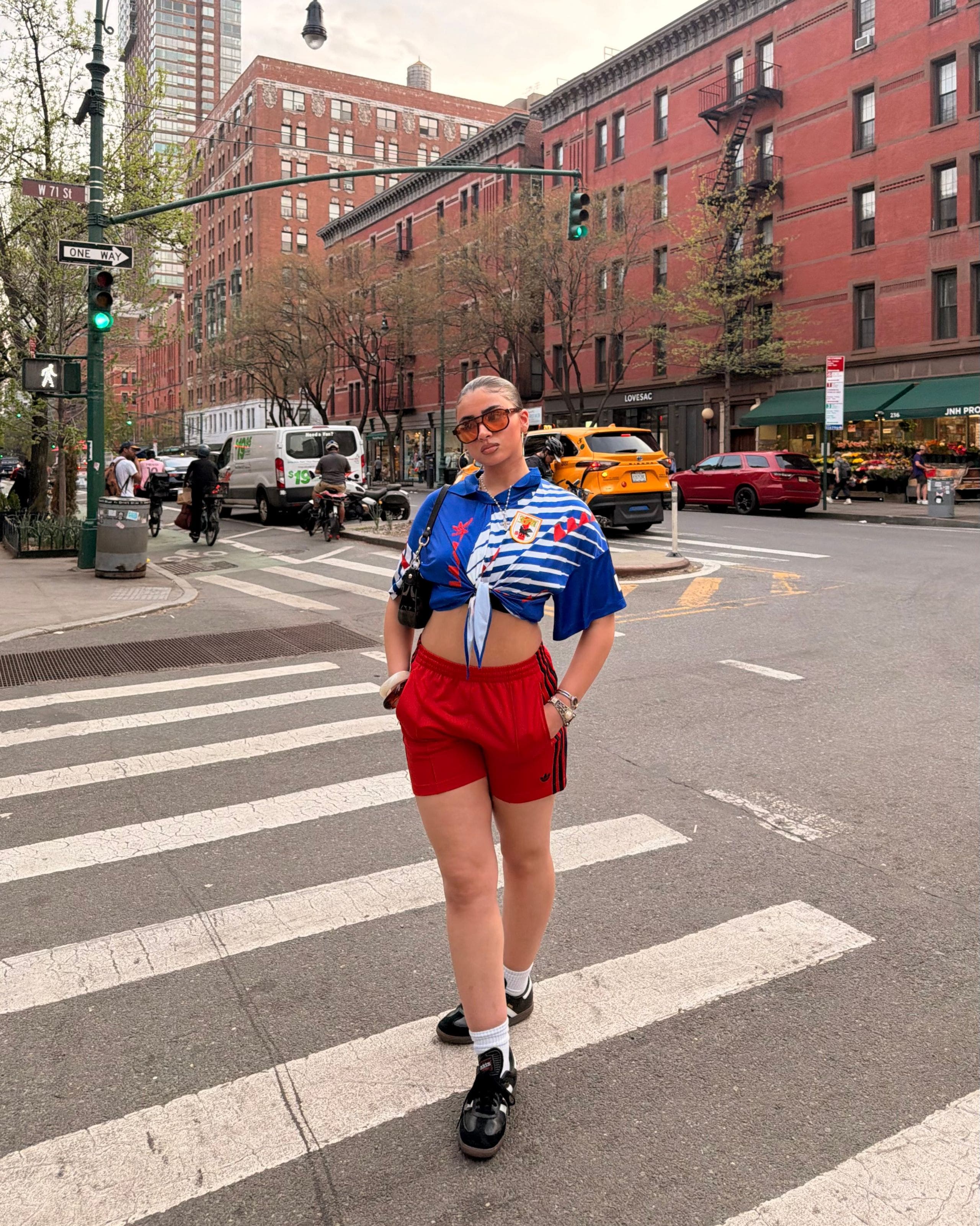 Woman wearing a collared soccer jersey and red shorts with Adidas sneakers.