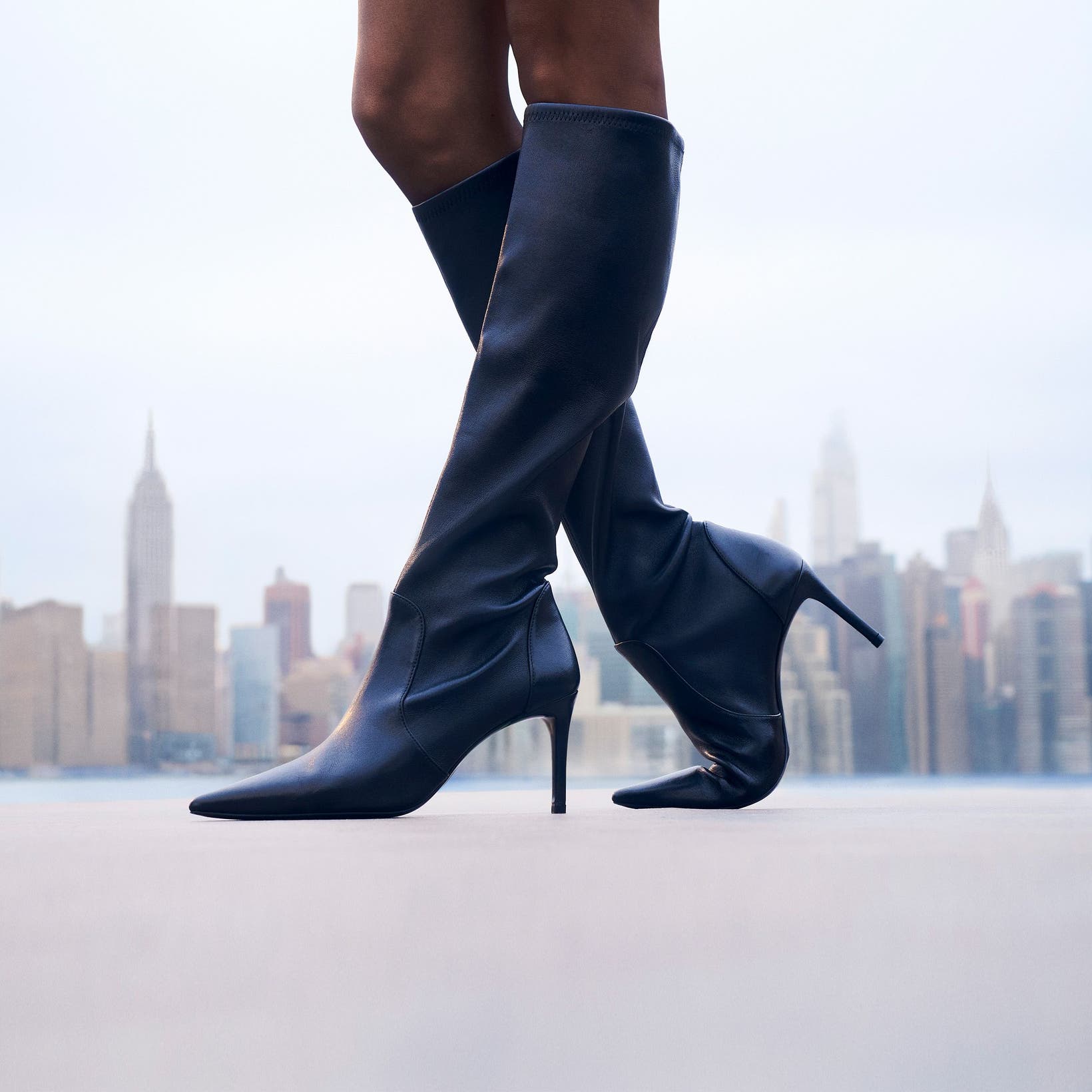 Woman wearing Stuart Weitzman knee-high boots in front of the New York skyline.