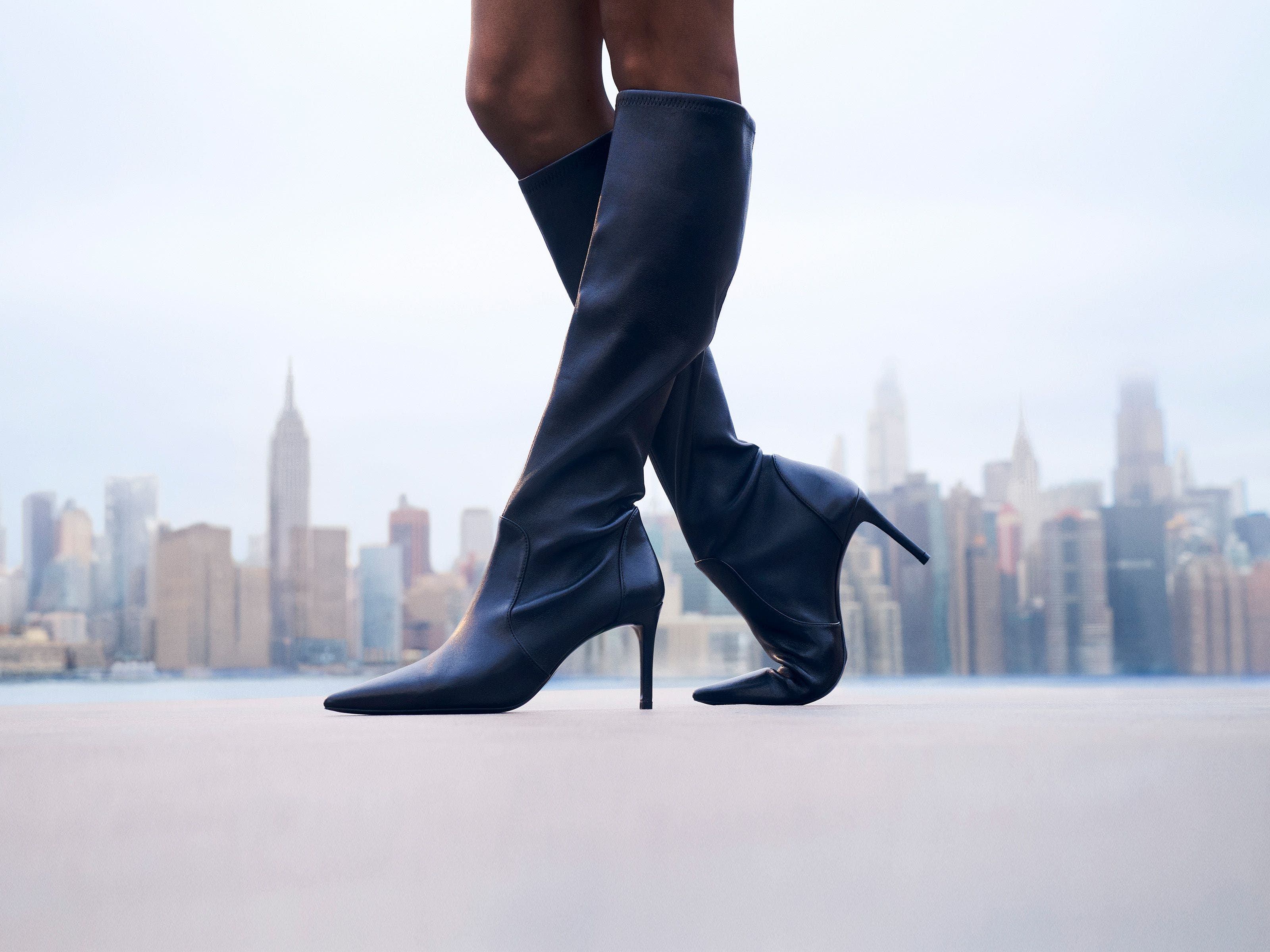 Woman wearing Stuart Weitzman knee-high boots in front of the New York skyline.