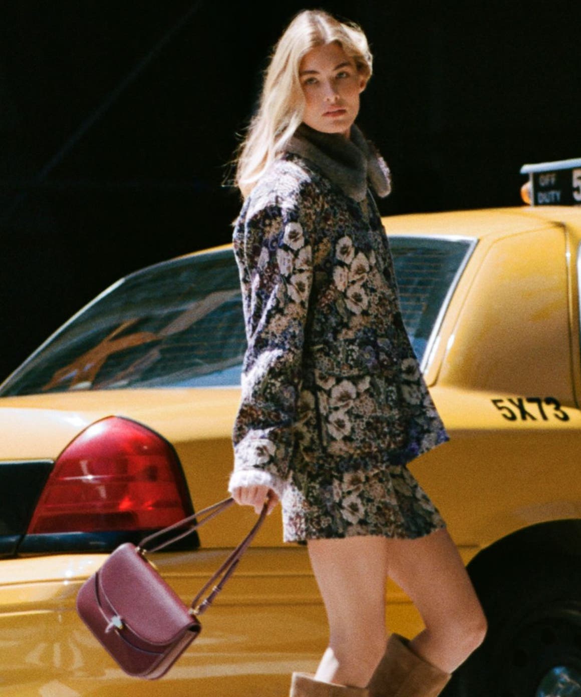 A woman wearing Veronica Beard and walking behind a taxi.