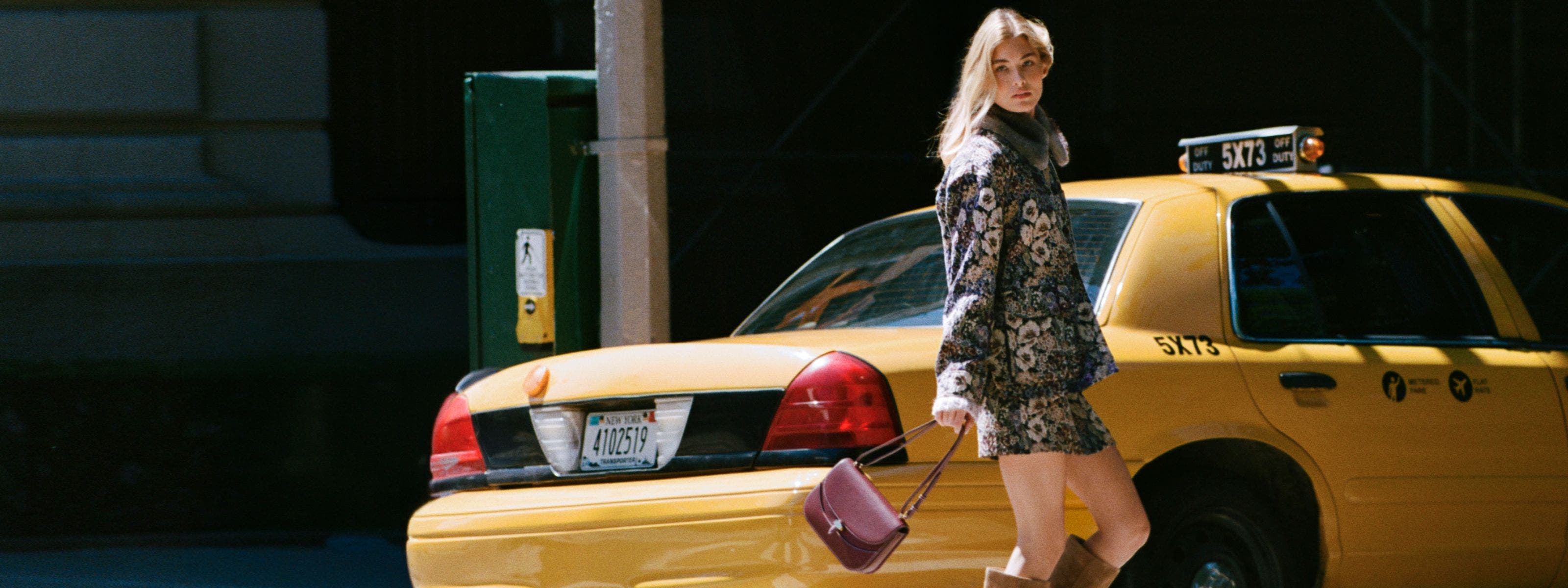A woman wearing Veronica Beard and walking behind a taxi.