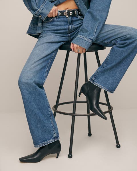 A woman wearing a denim shirt, jeans and black boots.
