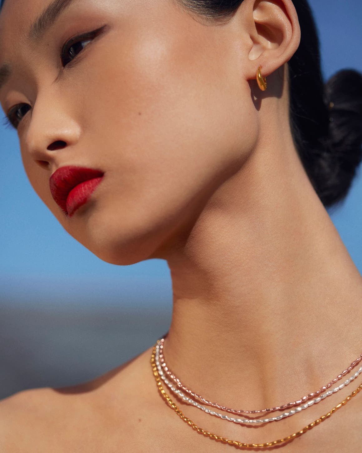 Woman wearing earrings and three necklaces in different colors from Monica Vinader.