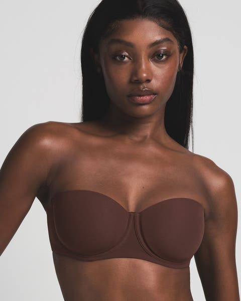 A woman wearing a SKIMS brown strapless bra.