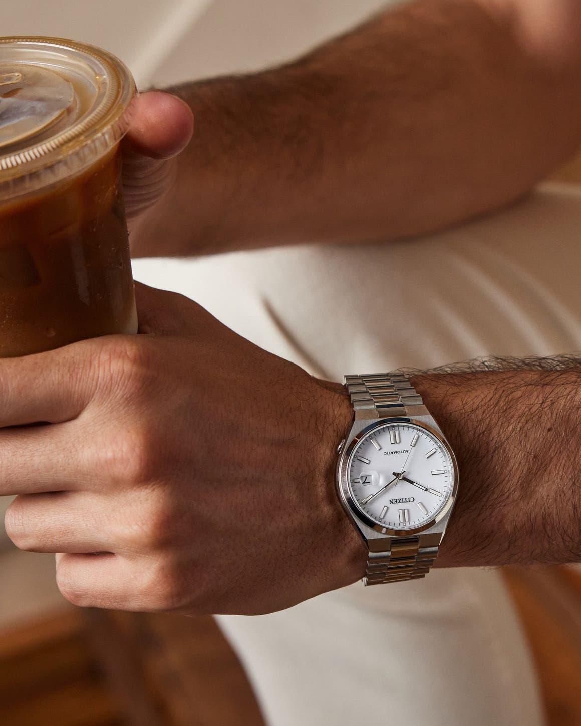 A man wearing a watch and holding an iced coffee.