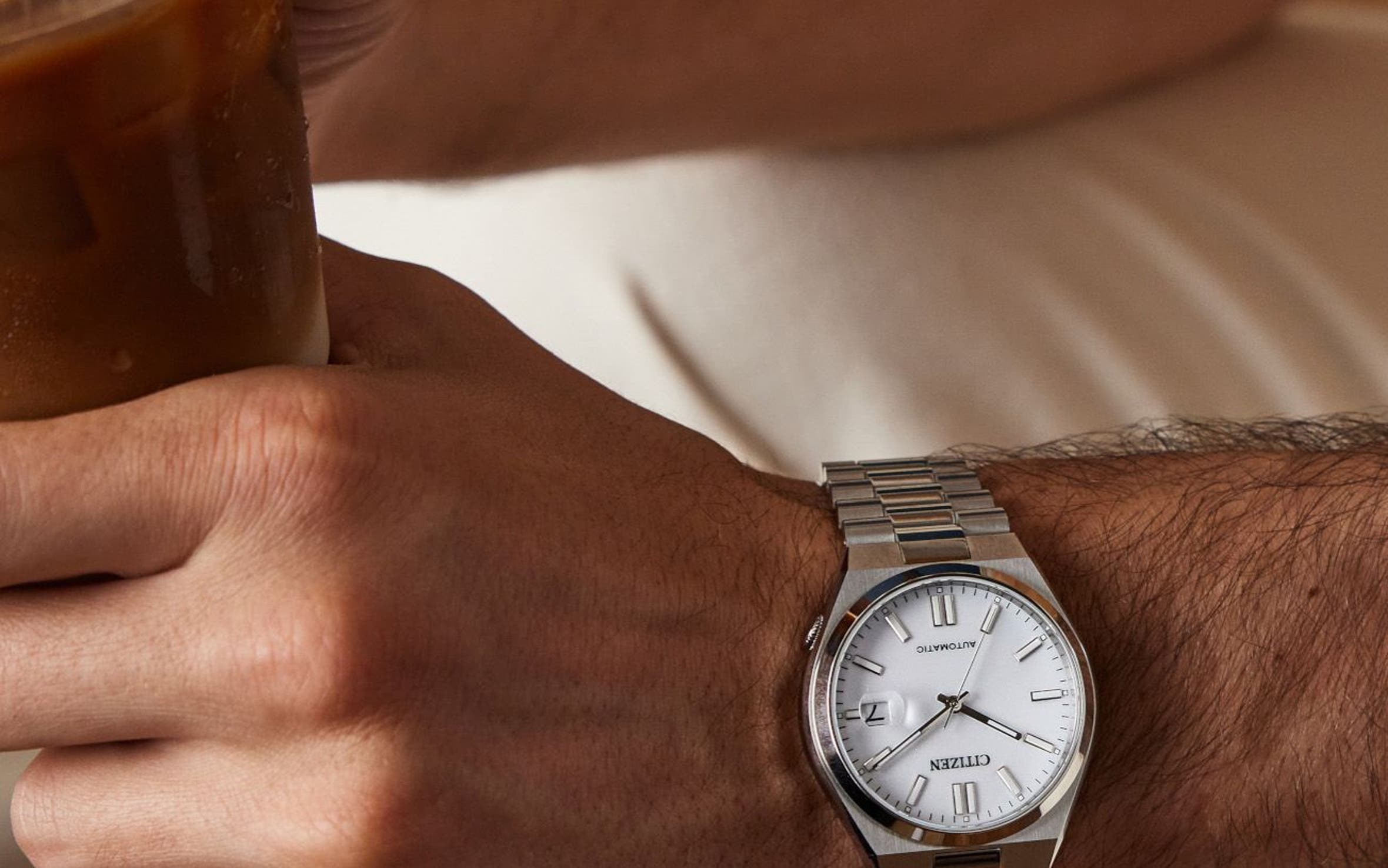 A man wearing a watch and holding an iced coffee.