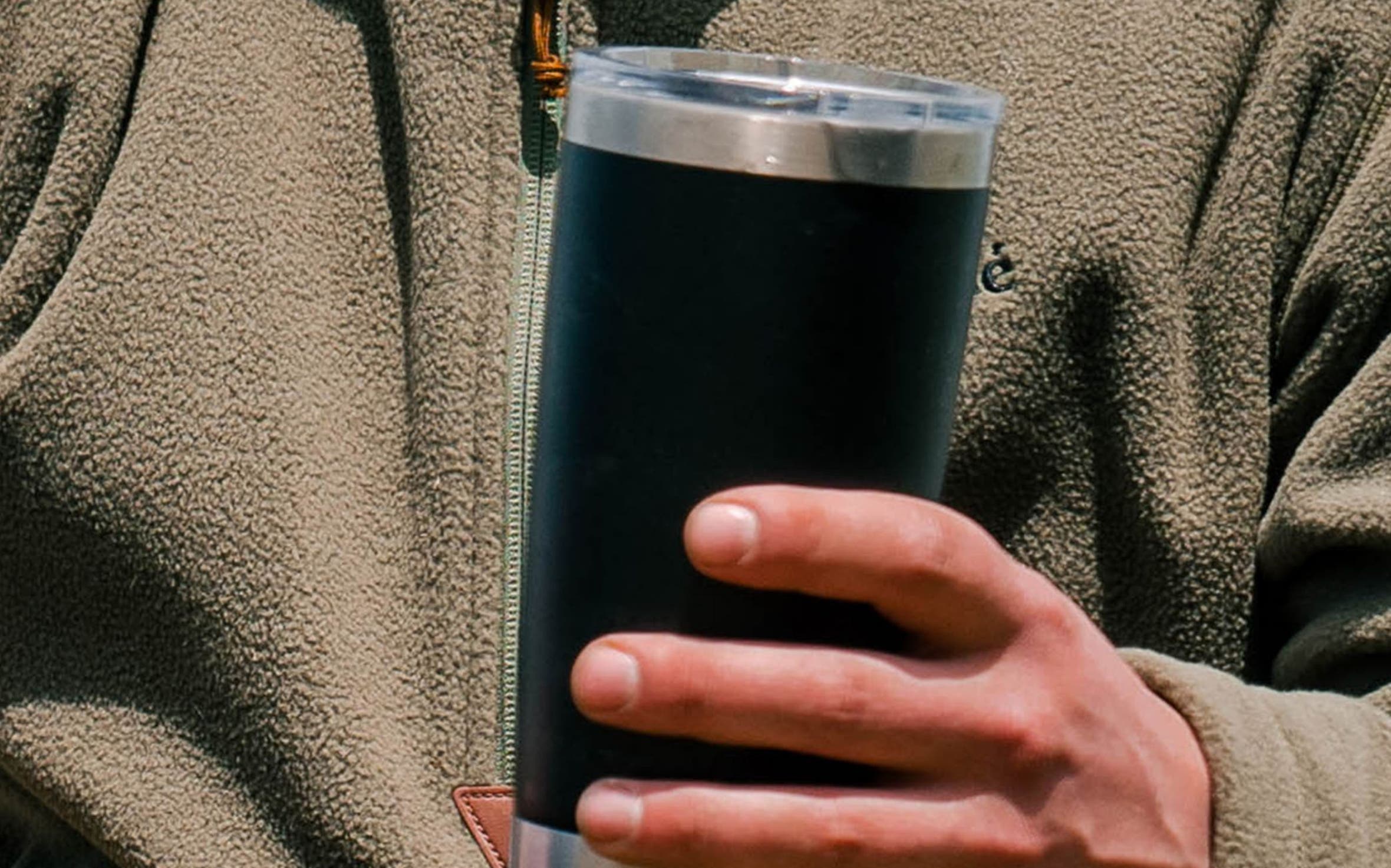 A man wearing a quarter-zip sweater and holding a travel mug. 