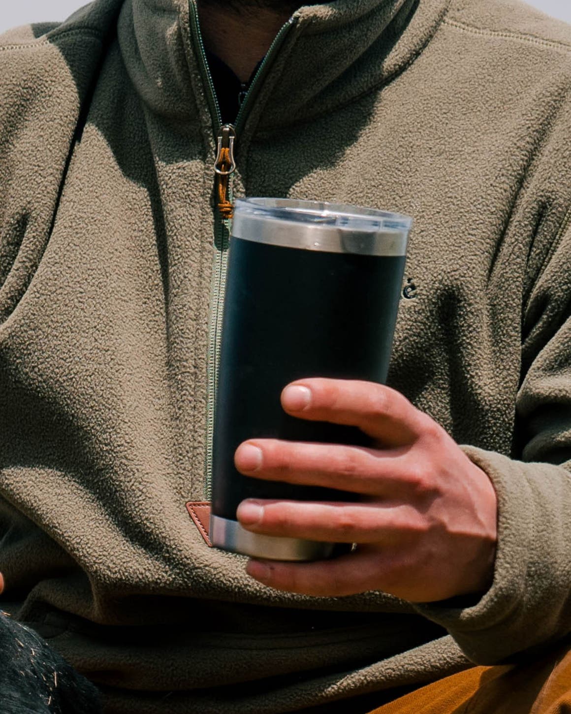A man wearing a quarter-zip sweater and holding a travel mug. 