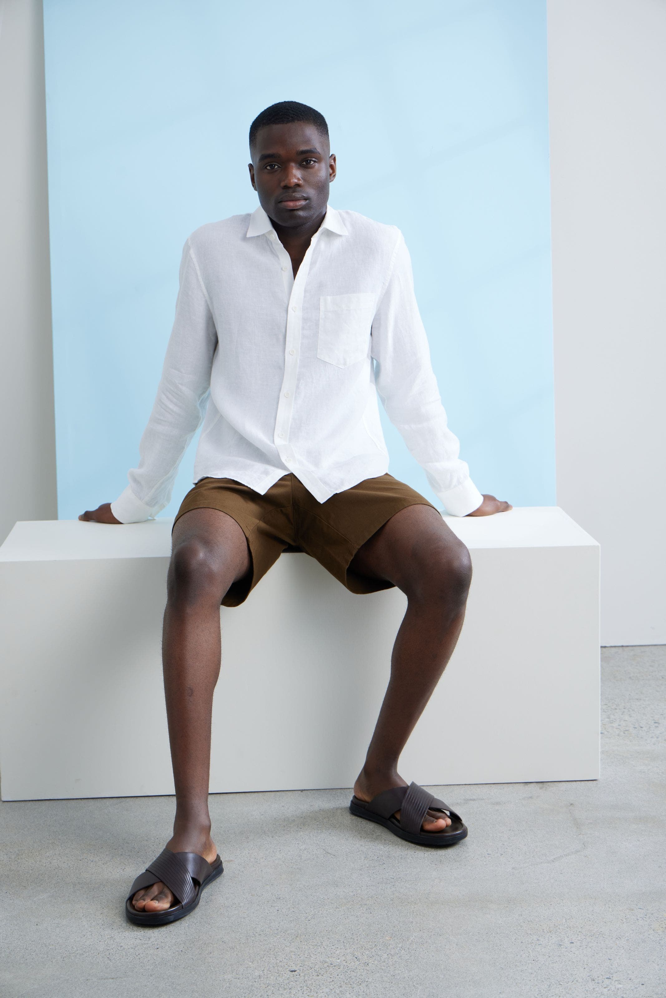 A man wearing a white button-up shirt and brown shorts.