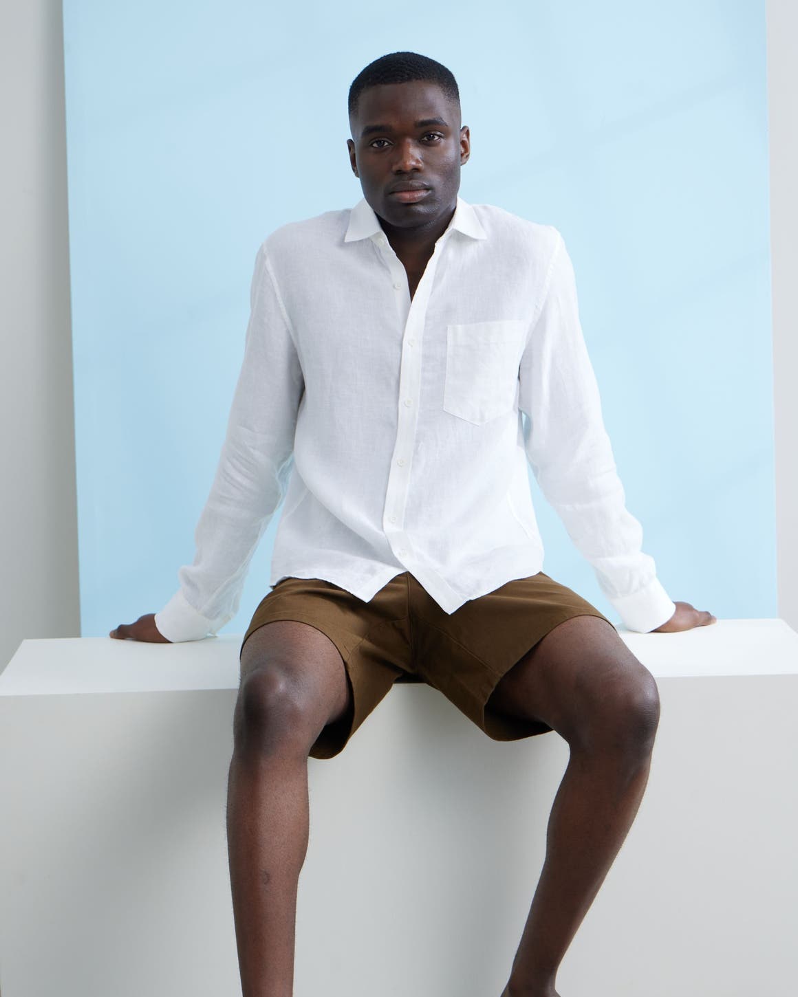A man wearing a white button-up shirt and brown shorts.